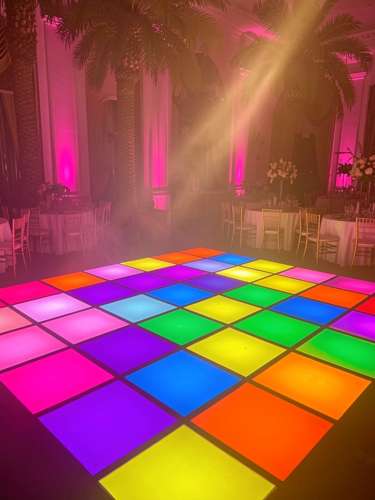 Piso de dança com 16 ladrilhos neon em grade, palmeiras ao fundo e luz rosa suave nas paredes, salão luxuoso e escuro.