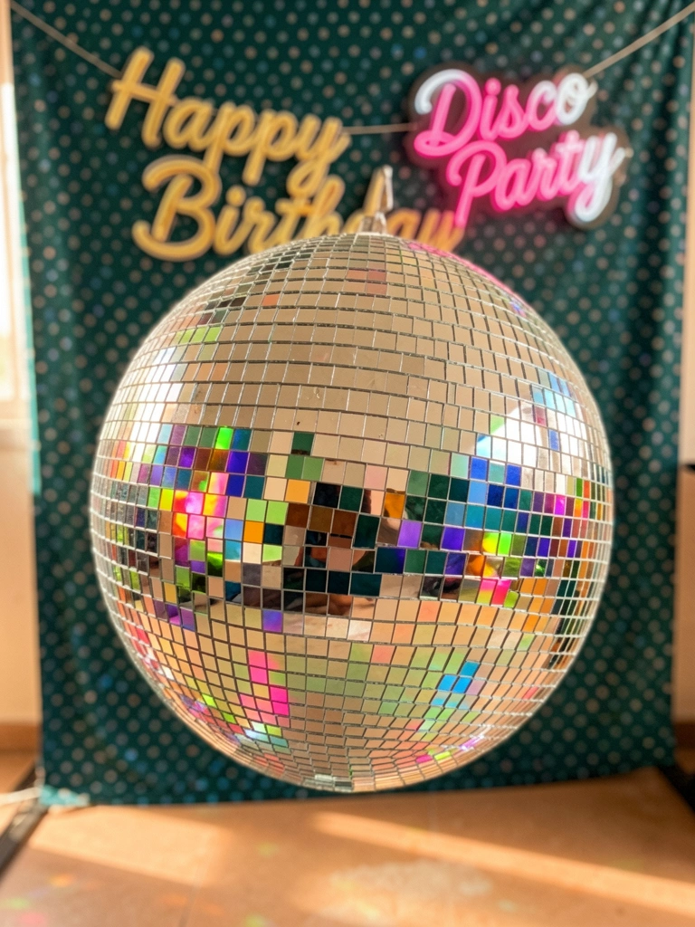 Close de bola de discoteca prateada refletindo luzes coloridas em fundo com banner 