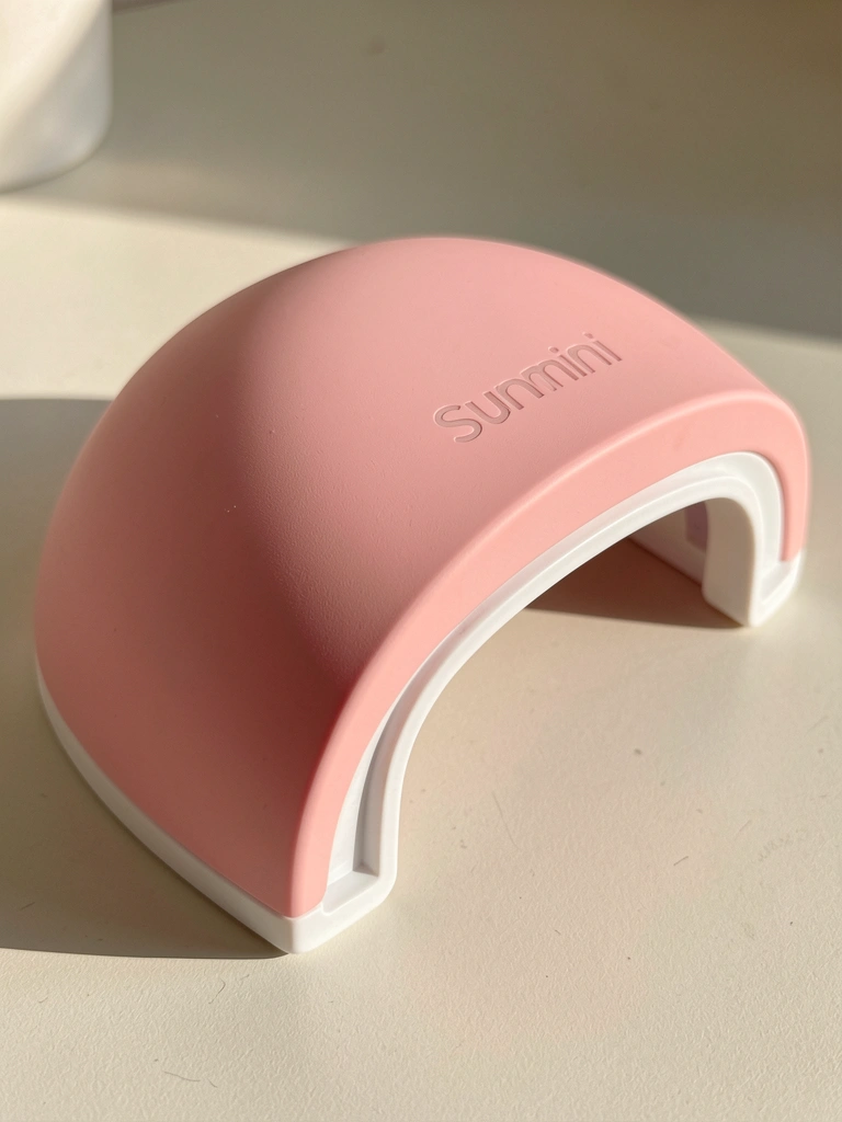 Luminária UVLED Sunmini rosa com superfície curva e suportes plásticos brancos, iluminação difusa e sombra suave.