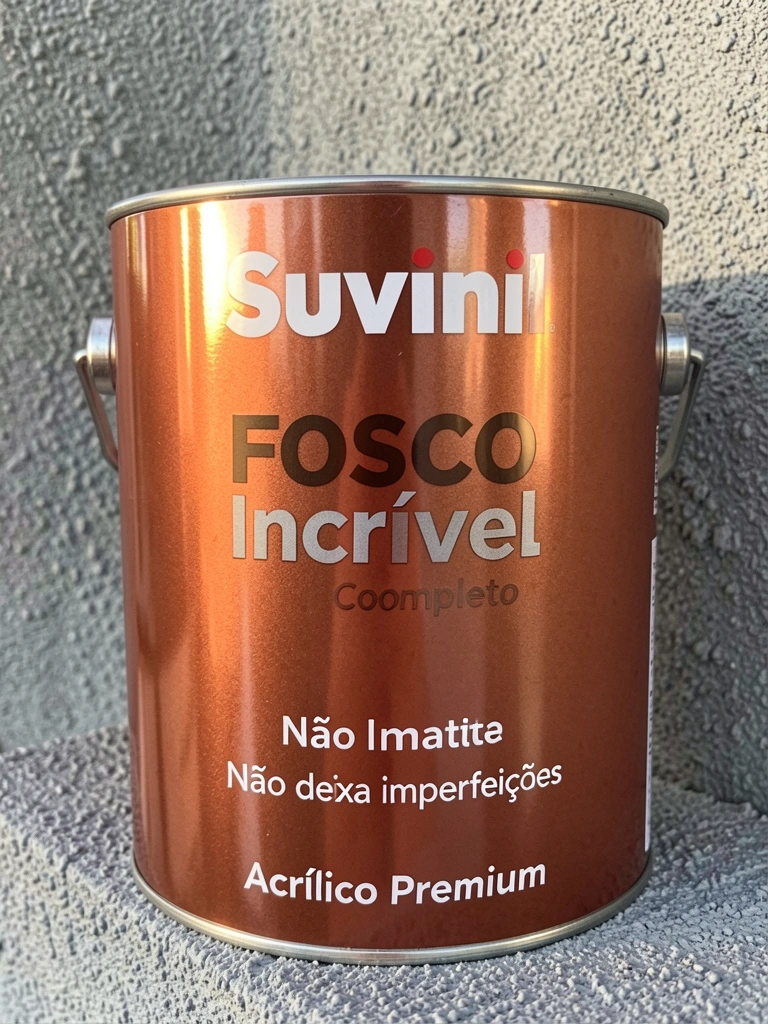 Lata de tinta Suvinil Fosco Completo em cobre metálico sobre parede texturizada cinza, com reflexos de luz natural e rótulo visível.