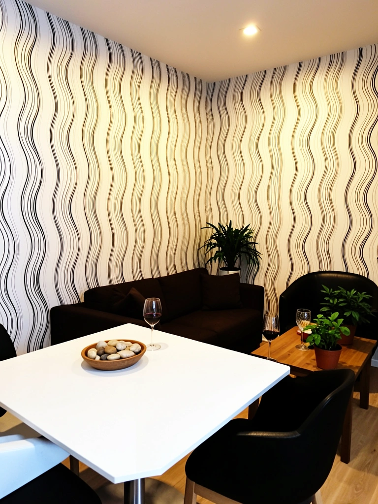 Papel de parede ondulado preto e branco domina sala com mesa branca de base prateada, sofá marrom e poltrona preta; vaso de planta e tigela com pedras decorativas sobre a mesa.