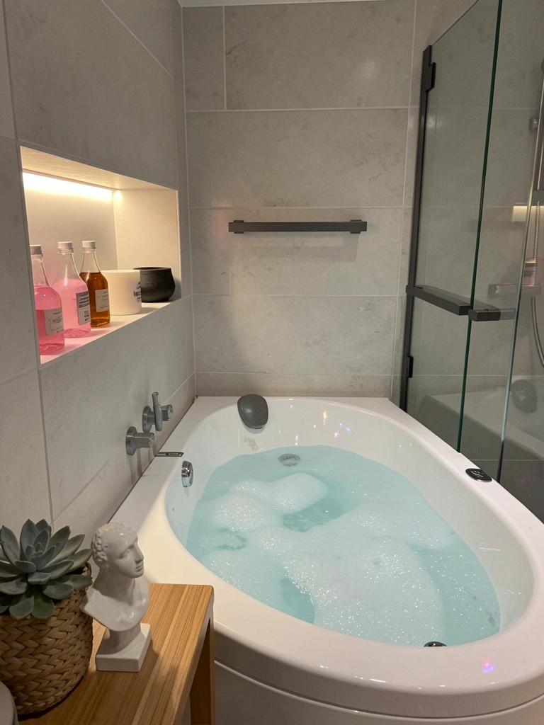Banheira com luzes LED nas cores azul e roxo, iluminação indireta ao redor e água com reflexos coloridos.