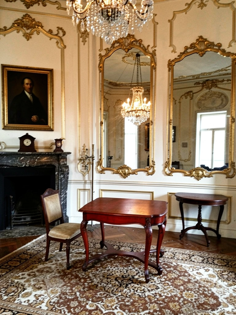 Sala com lustre de cristal, espelho dourado ornamentado e móveis esculpidos em madeira escura.