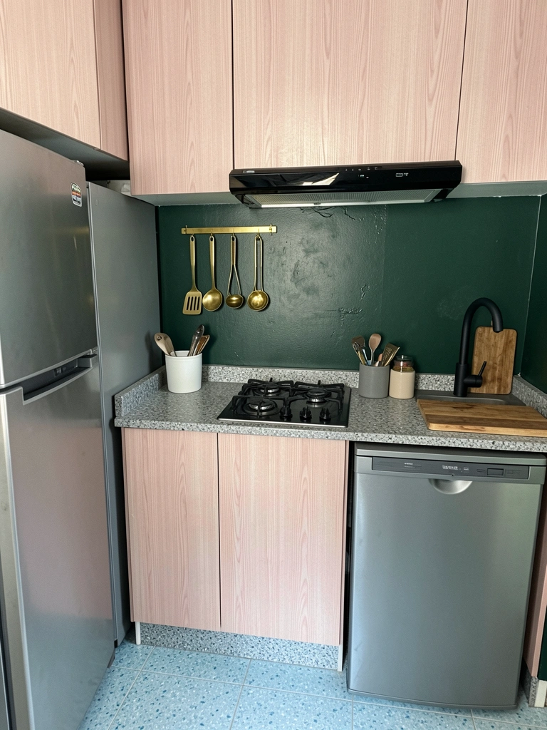 Parede verde-escura com utensílios dourados pendurados em cozinha compacta