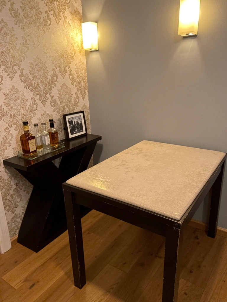 Sala de estar com sofá cinza, mesa de centro de madeira e arandelas de parede acesas, criando luz indireta nas paredes claras.