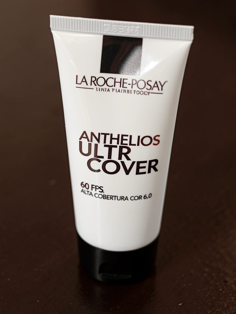 Tubo de protetor solar La Roche-Posay Anthelios Ultra Cover branco com tampa preta sobre superfície marrom-escura, iluminação suave e foco nítido.