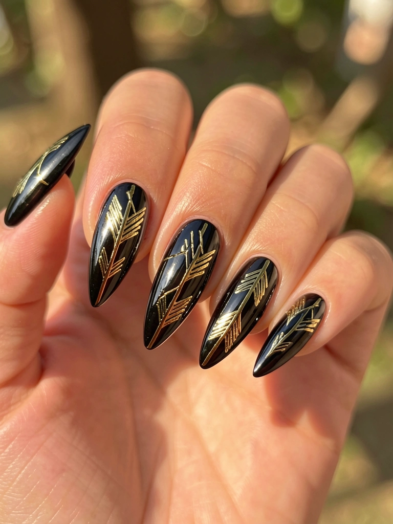 Mão com unhas pretas e detalhes dourados em forma de flecha, luz natural e fundo desfocado.