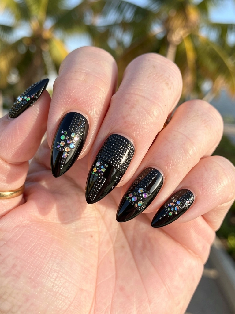Mão com unhas pretas em gel decoradas com pedras brilhantes e glitter, anel de ouro fino, luz natural quente.