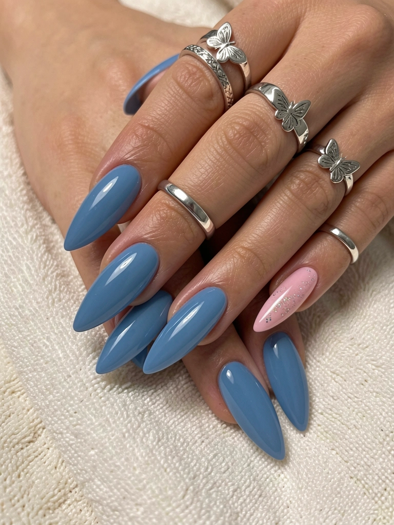 Mãos femininas com unhas azuis em gel, formato amendoado, anéis de prata com borboletas, sobre tecido off-white texturizado, iluminação suave.